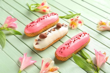Delicious eclairs and beautiful flowers on green wooden background