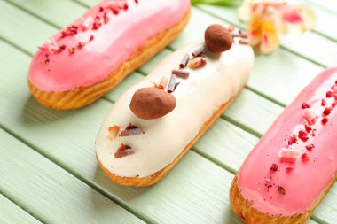 Delicious eclairs and beautiful flowers on green wooden background, closeup