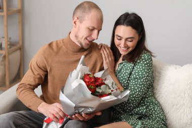 Young man greeting his wife with bouquet of flowers at home on Valentine's Day