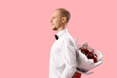 Young man with bouquet of flowers on pink background. Valentine's Day celebration