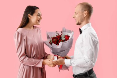 Young man with flowers and ring proposing to his girlfriend on pink background. Valentine's Day celebration