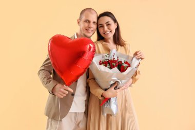 Young couple with bouquet of flowers and balloon on beige background. Valentine's Day celebration