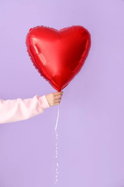 Woman with heart shaped balloon for Valentine's Day on lilac background