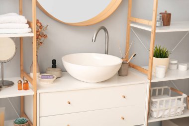 Ceramic sink, vase with dried flowers and bath accessories on drawers in bathroom