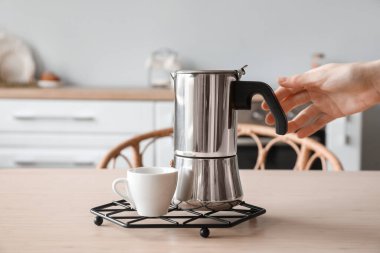 Grid with geyser coffee maker and cup on table in kitchen