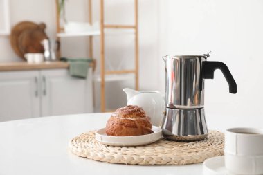 Geyser coffee maker with delicious bun and cup of espresso on table in kitchen