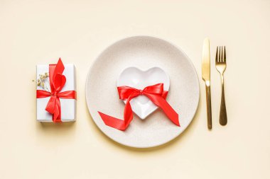 Table setting for Valentine's Day with gift on beige background
