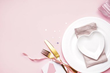 Table setting for Valentine's Day with envelope on pink background