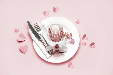 Table setting for Valentine's Day with glass and hearts on pink background
