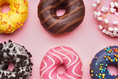Assortment of delicious donuts on pink background, closeup
