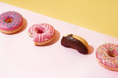 Different delicious donuts on pink table near yellow wall