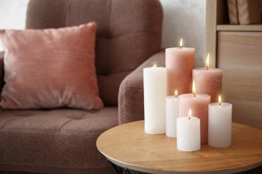 Interior of living room with burning candles on coffee table and cozy armchair with cushion