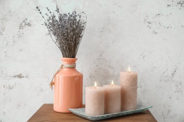 Burning candles and vase with lavender on table near grunge wall