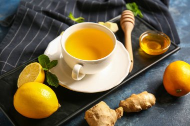 Board with cup of tea, mint, ginger and honey on dark grunge background