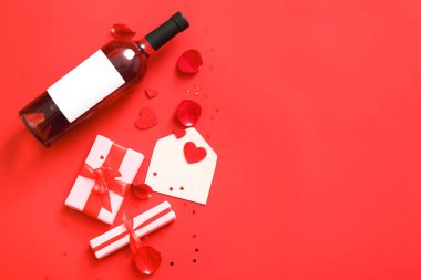 Composition with bottle of wine, gifts, envelope and rose petals on red background. Valentines Day celebration