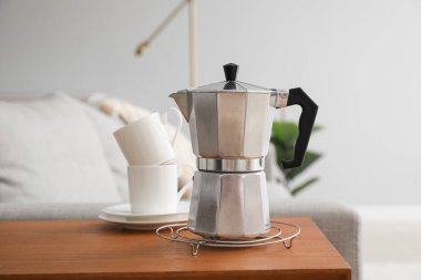 Grid with geyser coffee maker and cups on table in living room