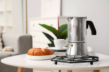 Grid with geyser coffee maker, cup of espresso and delicious croissant on table in living room