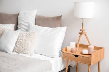 Burning candles and lamp on end table in bedroom near bed