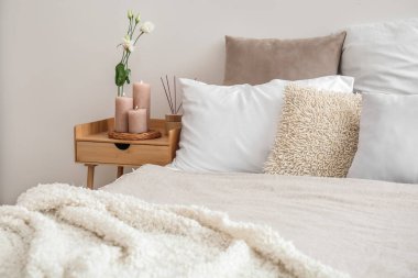 Burning candles, eustoma flower and reed diffuser on end table in bedroom