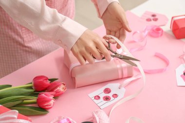 Woman packing beautiful gift box for International Women's Day celebration at table