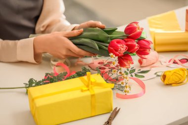Female hands with beautiful flowers and gift box at table, closeup. International Women's Day celebration