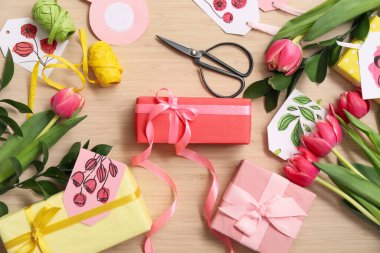 Composition with gift boxes, tulip flowers and packing materials on wooden background.  International Women's Day celebration