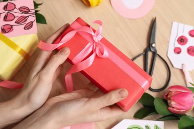 Female hands with beautiful gift for International Women's Day celebration on wooden background, closeup