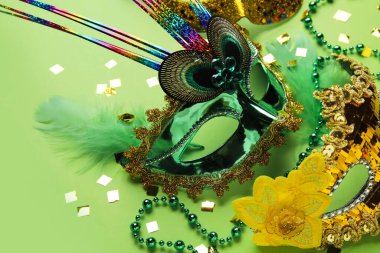 Carnival masks for Mardi Gras celebration with beads and confetti on green background, closeup