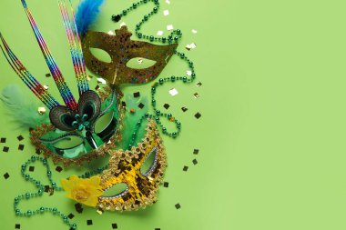 Carnival masks for Mardi Gras celebration with beads and confetti on green background