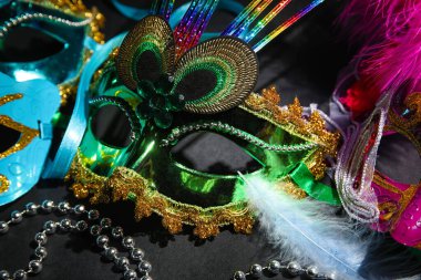 Carnival masks with beads for Mardi Gras celebration on dark background, closeup