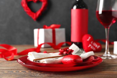 Red plate with cutlery, napkin and heart figure on wooden table. Valentine's Day celebration