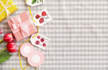 Gift boxes with paper tags and tulips for International Women's Day on checkered fabric background