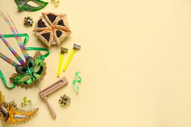 Hamantaschen cookies, carnival masks and noise makers for Purim holiday on yellow background