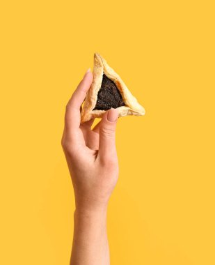 Woman with Hamantaschen cookie for Purim holiday on orange background