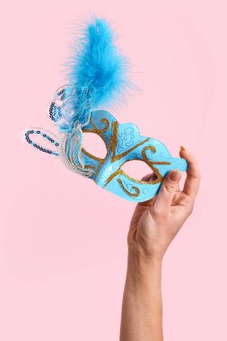 Woman with carnival mask for Purim holiday on pink background