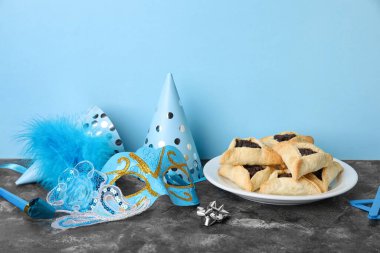 Hamantaschen cookies, carnival mask and party hats for Purim holiday on table near blue wall