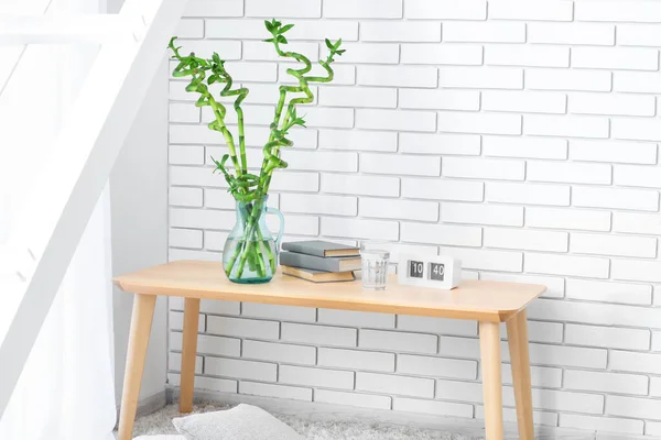 Vase with bamboo branches, books, glass of water and calendar on table near light brick wall
