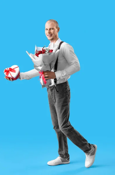 Young man with bouquet of flowers and gift on blue background. Valentine\'s Day celebration