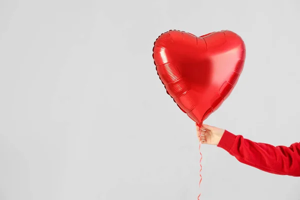 Woman with heart shaped balloon for Valentine's Day on light background