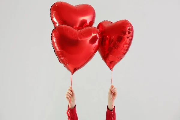Woman with heart shaped balloons for Valentine's Day on light background