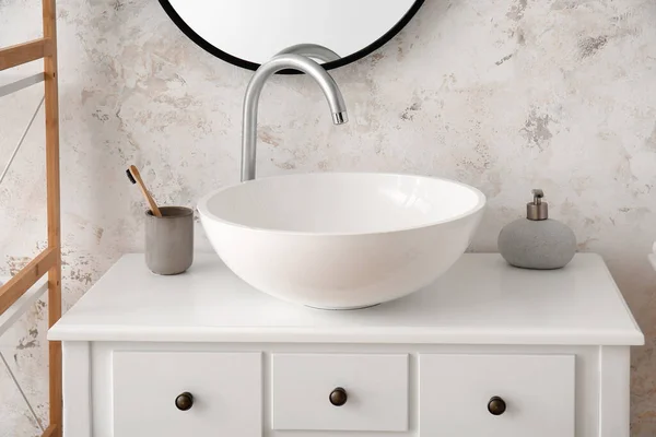 Ceramic sink, holder with toothbrush and soap on table in bathroom