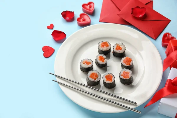 Plate with sushi rolls, chopsticks, envelopes and gifts on blue background, closeup. Valentine\'s Day celebration