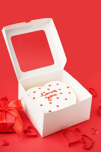 Opened box with tasty bento cake, gift and hearts on red background. Valentine\'s Day celebration