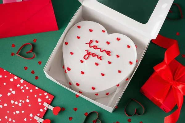 Opened box with heart-shaped bento cake and gift on green background. Valentine\'s Day celebration