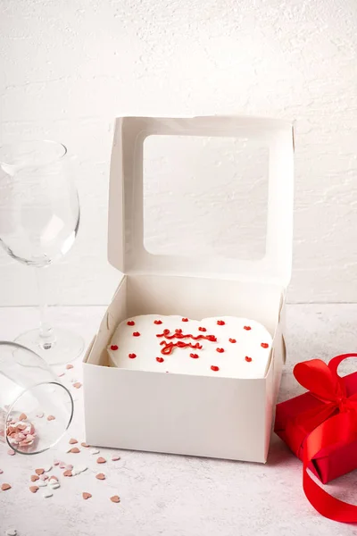 Box with tasty bento cake, glasses and gift on white table. Valentine\'s Day celebration