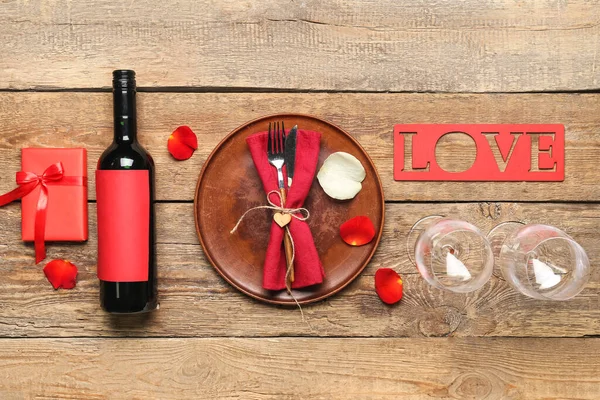 Table setting with bottle of wine, word LOVE, glasses and gift on wooden background. Valentine\'s Day celebration