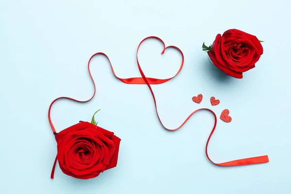 Rose flowers and heart made of red satin ribbon on blue background. Valentine\'s Day celebration