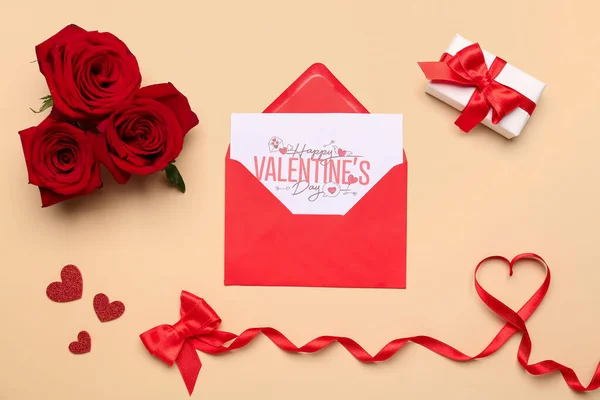 Composition with greeting card in envelope, rose flowers and heart made of red satin ribbon on beige background. Valentine\'s Day celebration