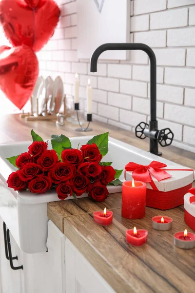 Sink with roses, wine glasses, burning candles and gifts for Valentine\'s Day on counter in kitchen