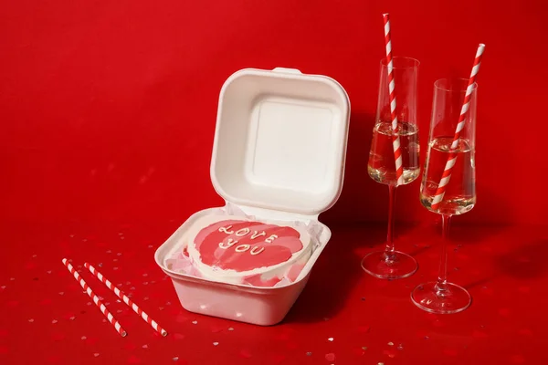Lunch box with bento cake, glasses of champagne and straws for Valentine\'s Day on red background